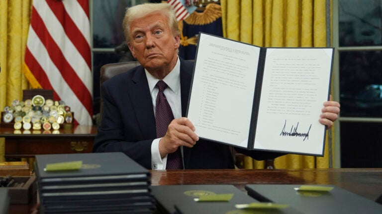 President Donald Trump holds up an executive order commuting sentences for people convicted of Jan. 6 offenses in the Oval Office of the White House, Monday, Jan. 20, 2025, in Washington.