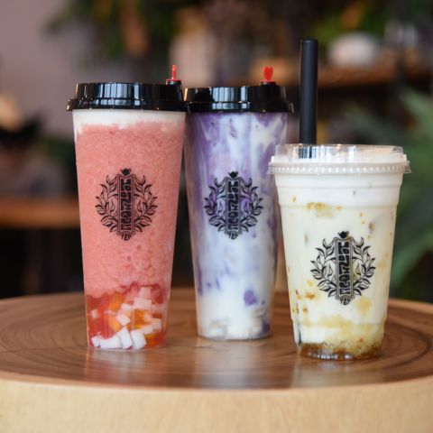 Three cups of flavored boba tea rest on small wooden table.