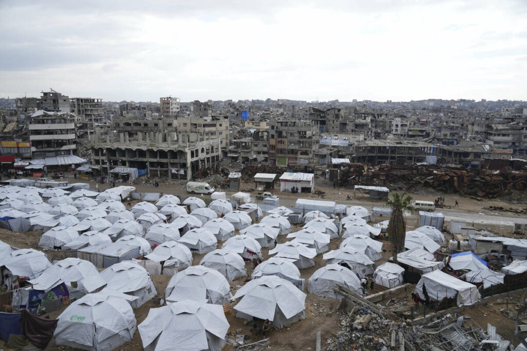 A sprawling tent camp for displaced Palestinians sits adjacent to destroyed homes and buildings ...