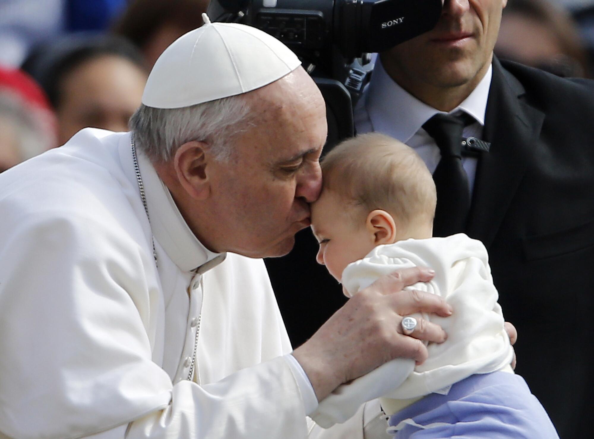 Pope Francis kisses a baby handed to him.