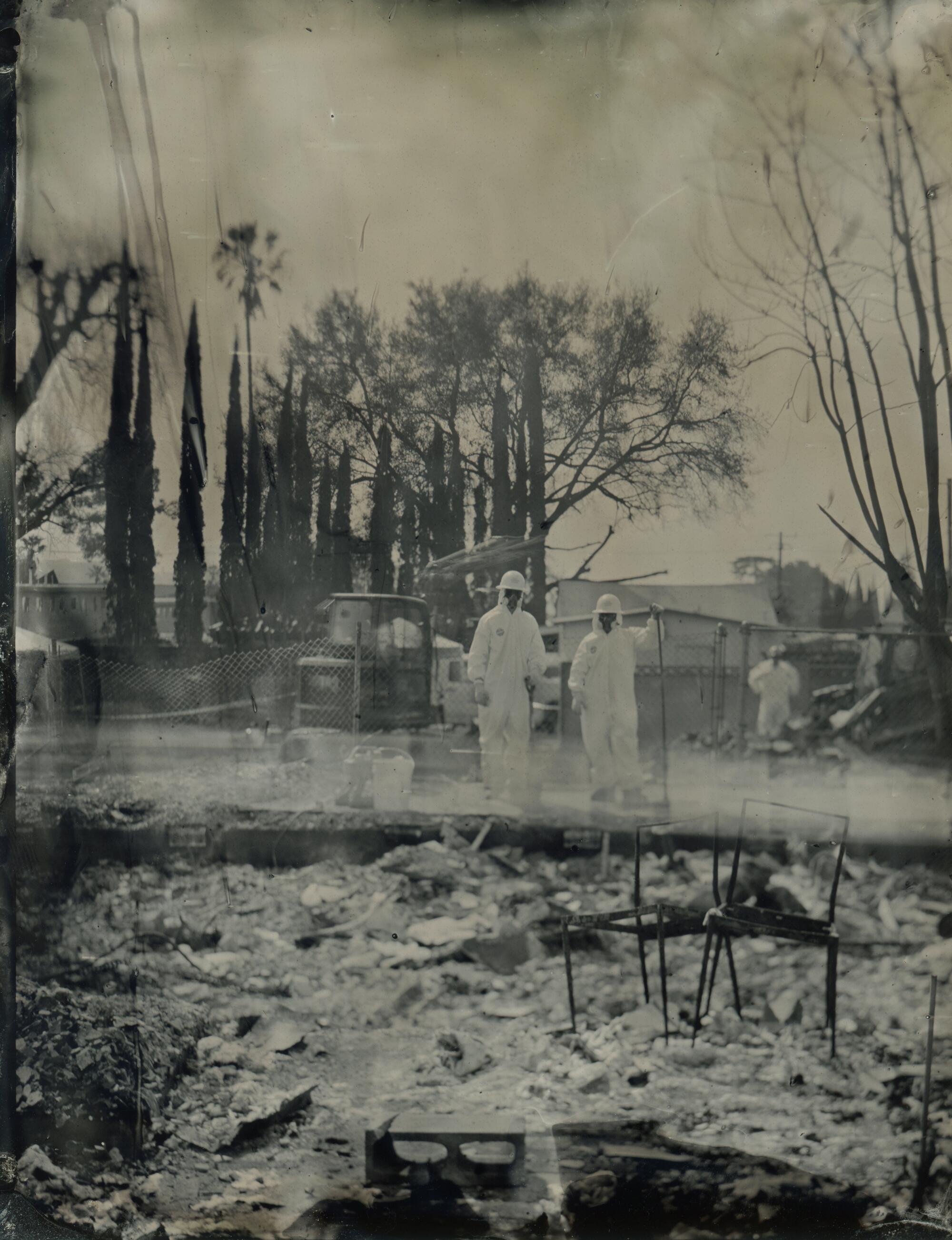 Two people in protective gear on a burned lot.