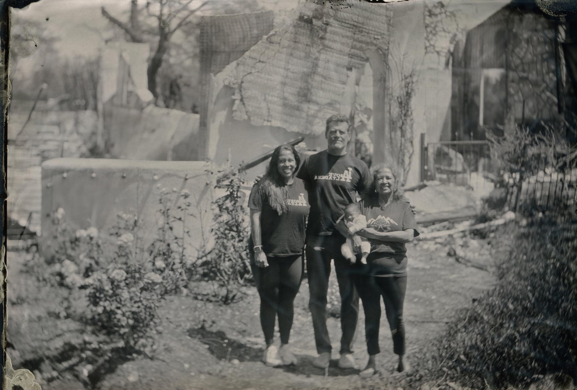 Three adults and a baby stand in front of a burned building