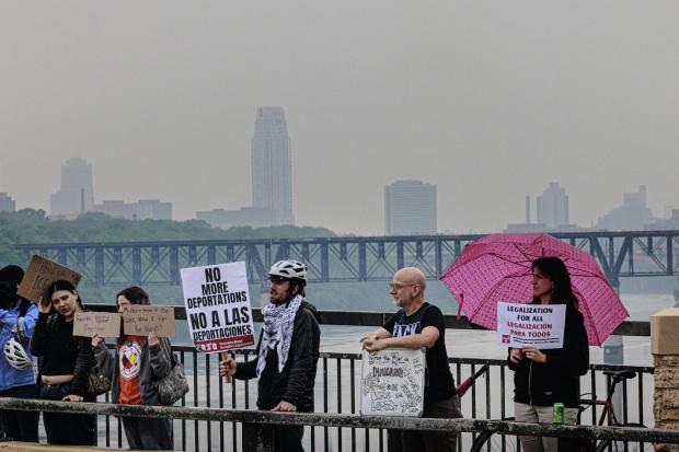 Demonstrators hold signs during a protest against recent immigration raids on the Lake Street-Marshall Bridge in Minneapolis