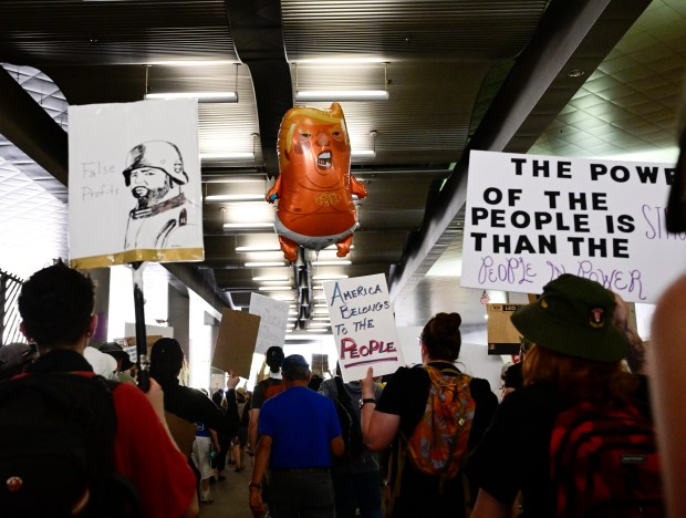 "No Kings" protesters march down Stout Street next to the...