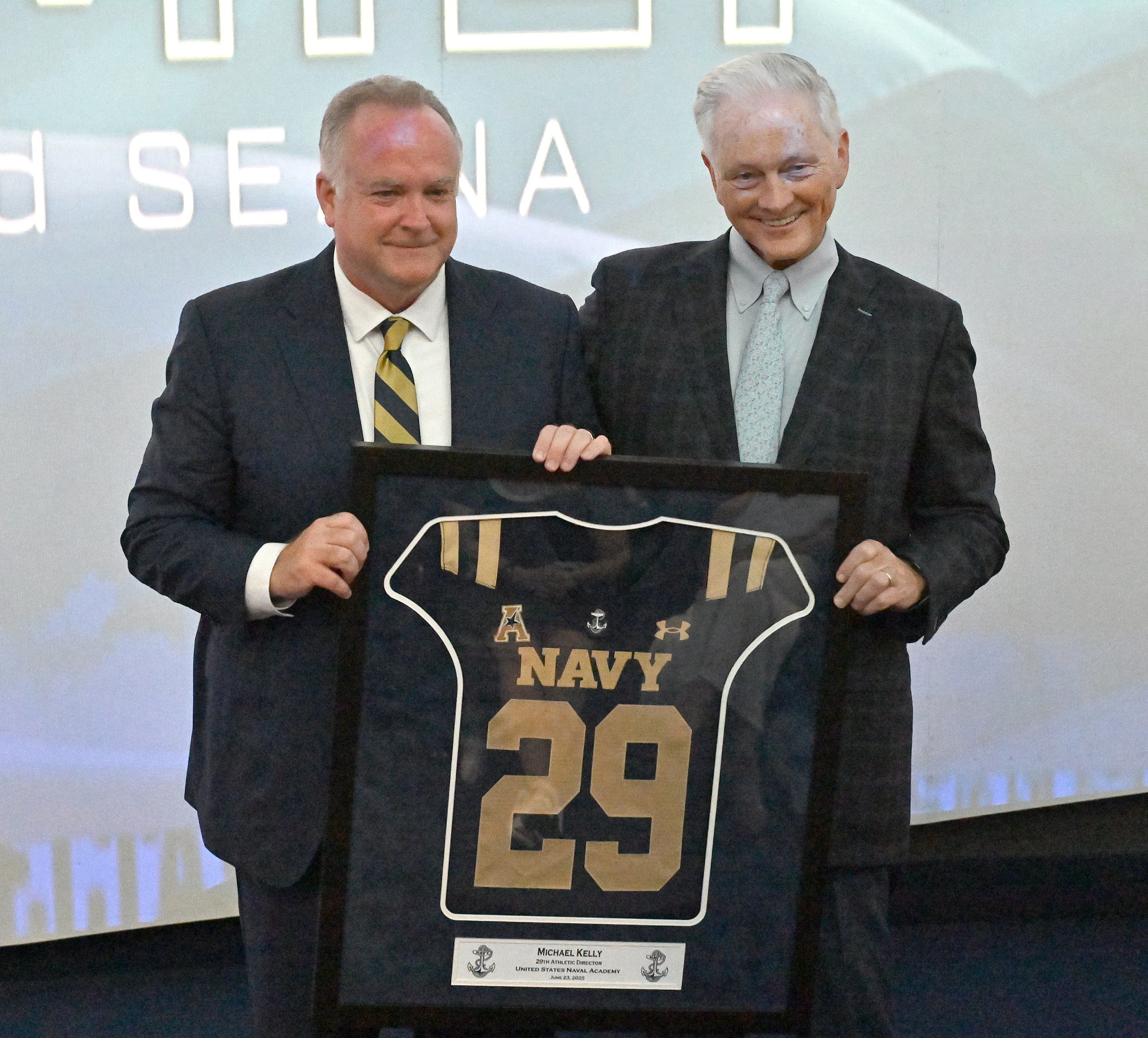 New Athletic Director Michael Kelly, left, gets a framed jersey from Chet Gladchuk. Outgoing Navy Athletic Director Chet Gladchuk said his goodbyes to staff today and introduced new Navy athletic director Michael Kelly during an event at academy. (Paul W. Gillespie/Staff)