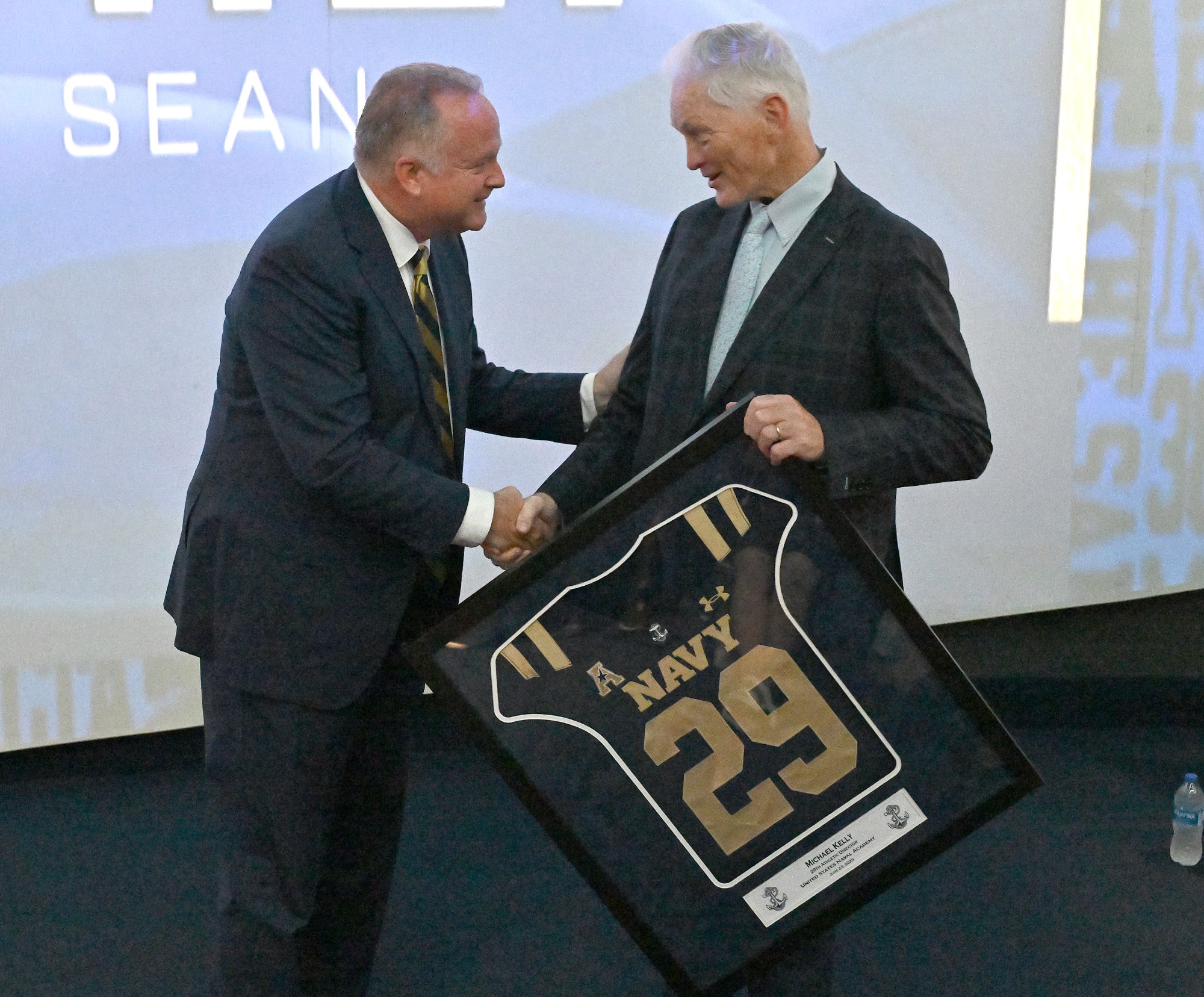 New Athletic Director Michael Kelly, left, gets a framed jersey from Chet Gladchuk. Outgoing Navy Athletic Director Chet Gladchuk said his goodbyes to staff today and introduced new Navy athletic director Michael Kelly during an event at academy. (Paul W. Gillespie/Staff)
