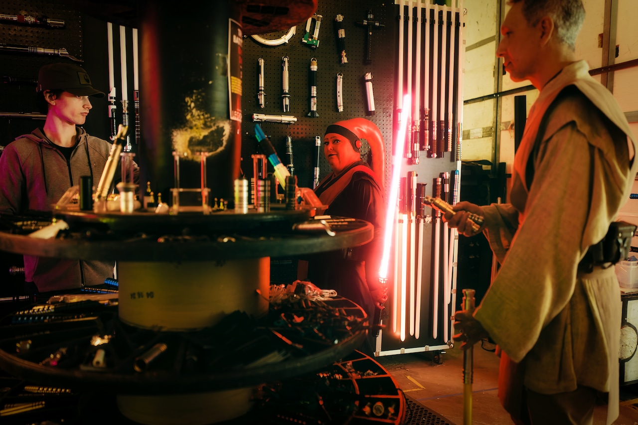 people in costume gather around a display of lightsabers for sale