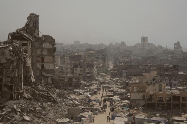 People walk along a street lined with destroyed buildings following...