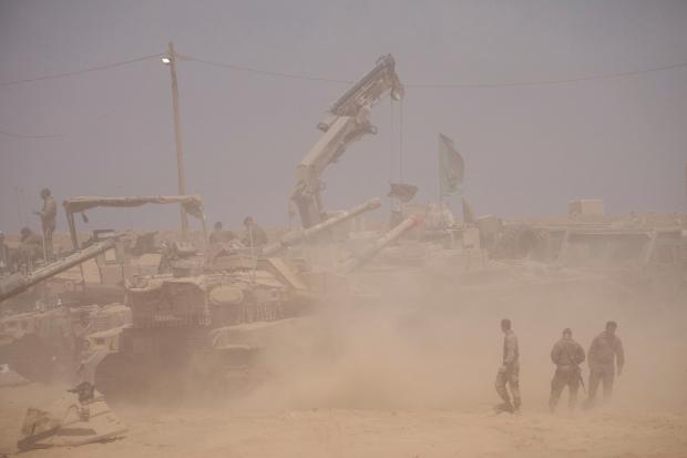 Israeli soldiers work on their tanks in a staging area...