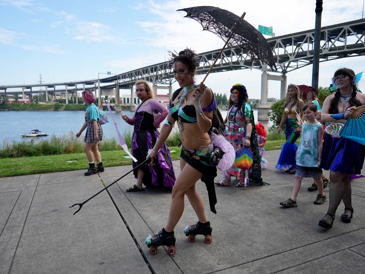 woman in mermaid inspired swimsuit holds a parasol and roller skates by in a parade