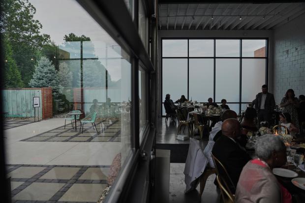 Guests sit inside during cocktail hour as empty chairs sit...