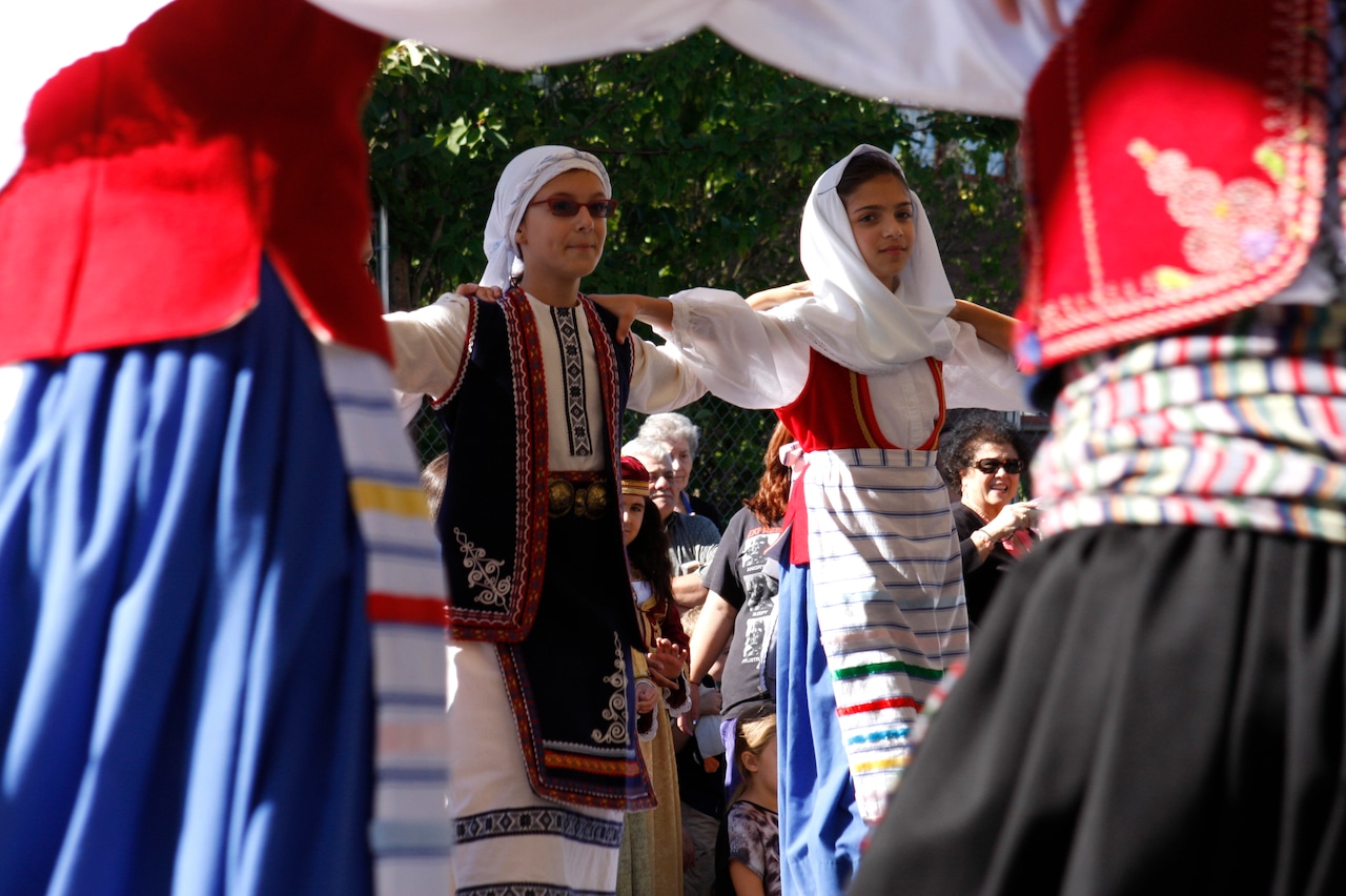 A close-up of two young dancers dressed in traditional Greek costume