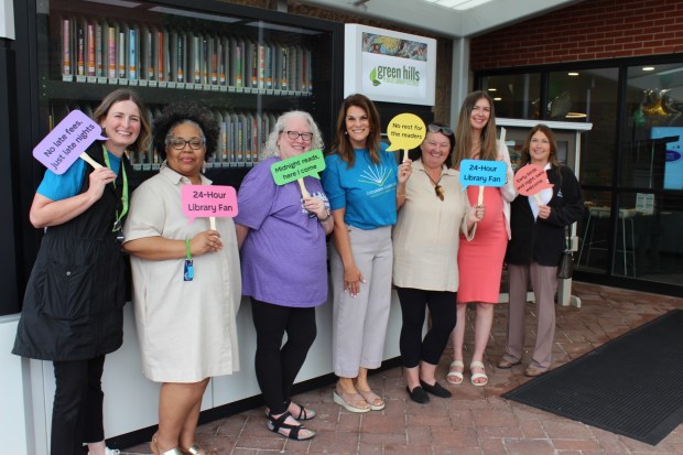 Patrons, city leaders and officials from Green Hills Public Library display novelty signs while standing in front of the state's first 24-hour library during an unveiling event Sept. 13 in Palos Hills. (Catherine Kruse)