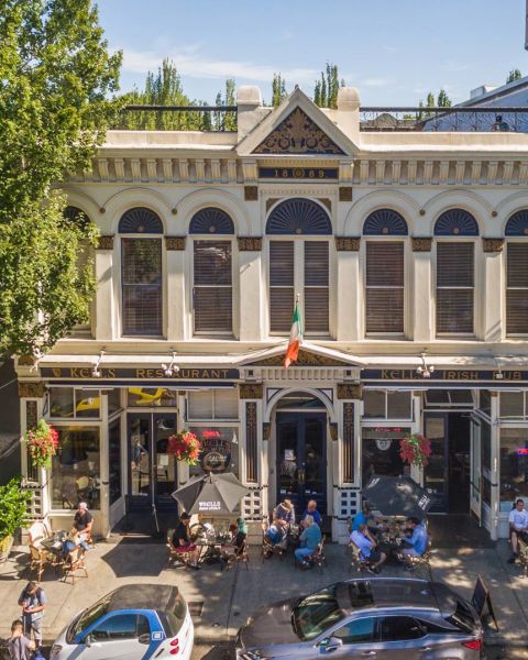 the facade of a large Irish pub with groups of people eating and drinking out front