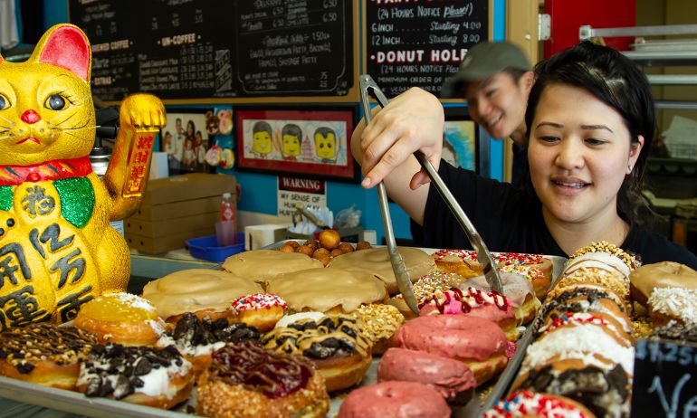 person using tongs to select a doughnut from a tray