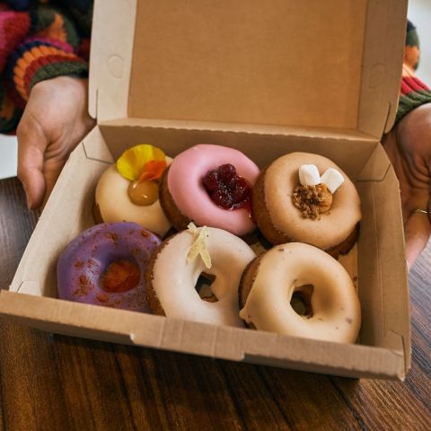 six doughnuts in a box with toppings such as marshmallows, raspberries and flower petals