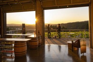 people stand on a patio sipping wine with a view of the valley as the sun sets