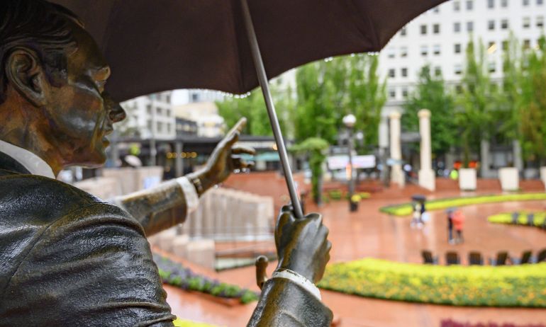 a statue of a man in a suit holding an umbrella in an urban park on a rainy day