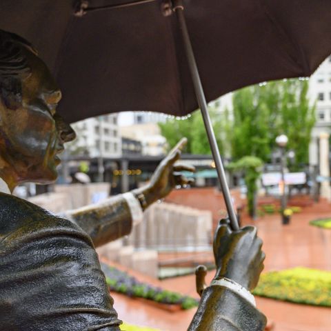 a statue of a man in a suit holding an umbrella in an urban park on a rainy day