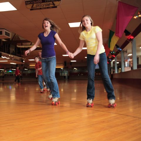 two people smile while holding hands and skating across a classic wooden roller rink