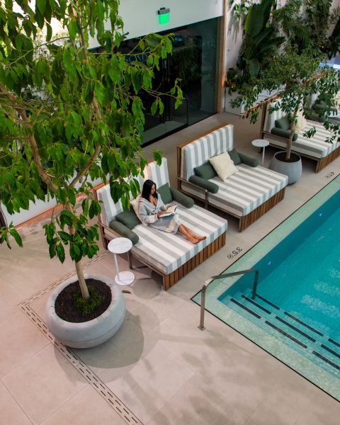 Woman in robe lounges next to a pool while reading a book.