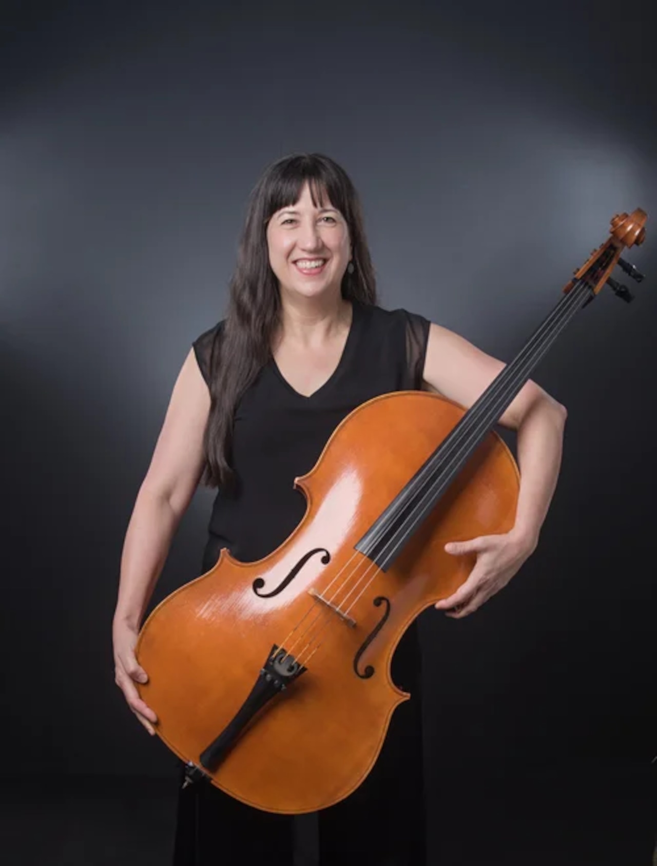 Nancy Ives is shown holding a cello in front of her