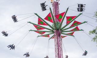 pink tower with colorful flags holding groups of two suspended in swings above the ground
