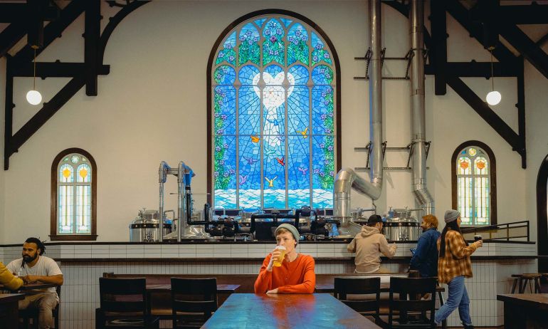 a person sips a beer in front of a stained glass window