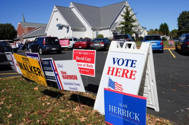 FILE - A Vote Here sign is posted amongst political signs as people arrive to vote at the Rutherford County Annex Building, an early voting site, Oct. 17, 2024, in Rutherfordton, N.C. (AP Photo/Kathy Kmonicek, File)