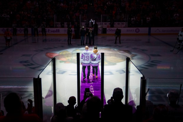 Fans and players applaud while radio analyst Troy Murray, who is currently battling cancer, walks on the ice with 15-year-old Devin Pittges, who is in remission from osteosarcoma, to drop the puck before the Chicago Blackhawks play the San Jose Sharks at the United Center on Nov. 28, 2021.