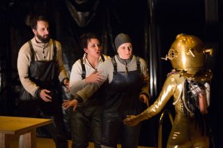 Three people in nautical gear and one in an old-fashioned diving suit perform on a stage