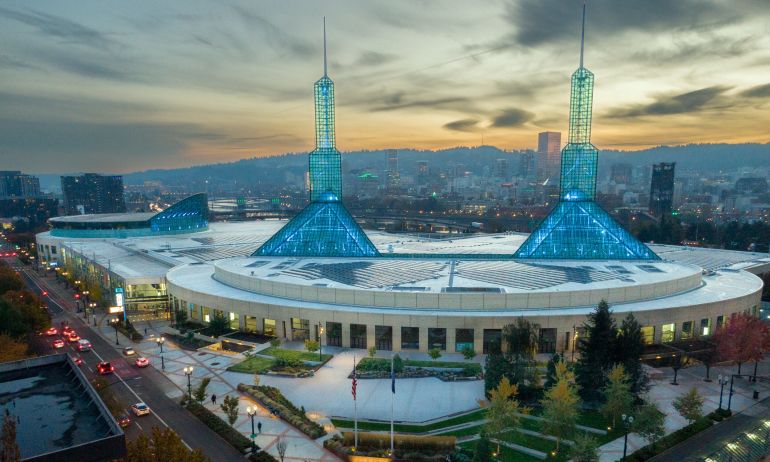 a vast building with two spires at sunset with the city skyline and hills in the background