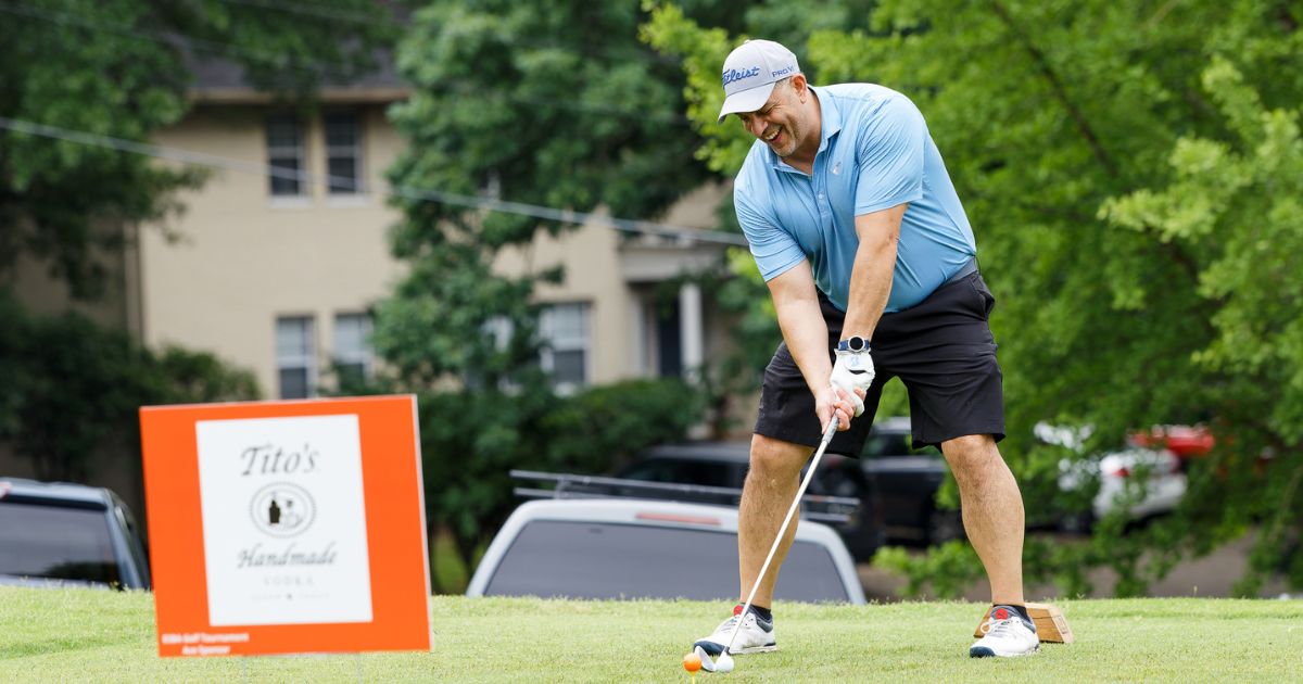 man in blue shirt teeing up a golf swing