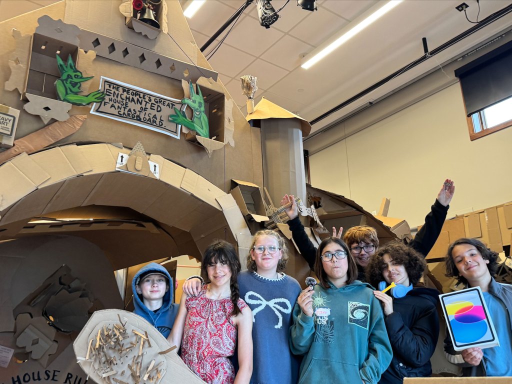 A group of middle school students stand next to a castle made of cardboard.