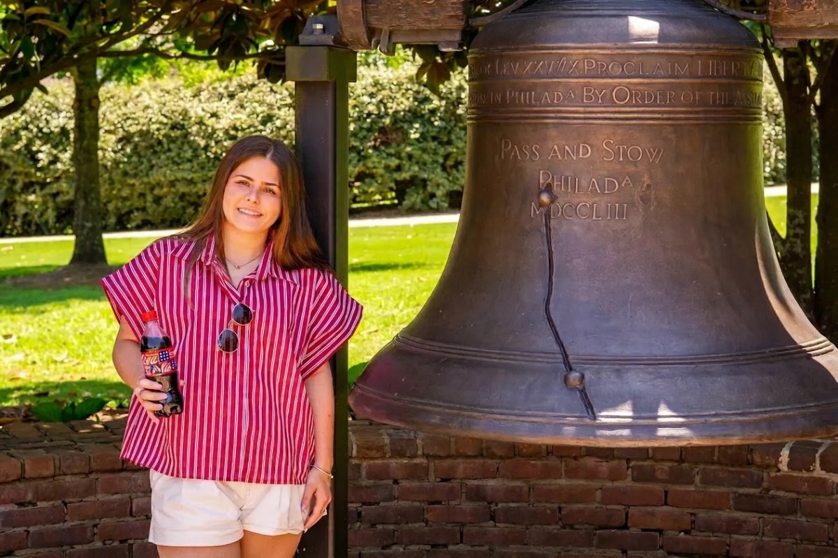 A woman in a red striped shirt poses beside a replica Liberty Bell at The American Village in Montevallo