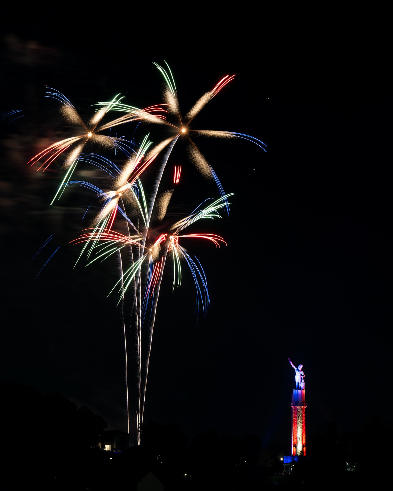 Red, white and blue fireworks burst in the night sky beside the illuminated Vulcan statue during Thunder on the Mountain