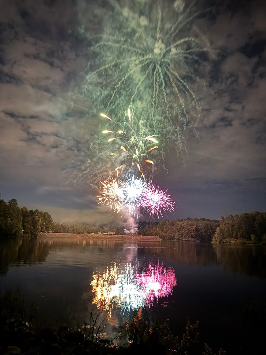 Fireworks bursting over the lake at Oak Mountain State Park, with colorful reflections shimmering on the water below