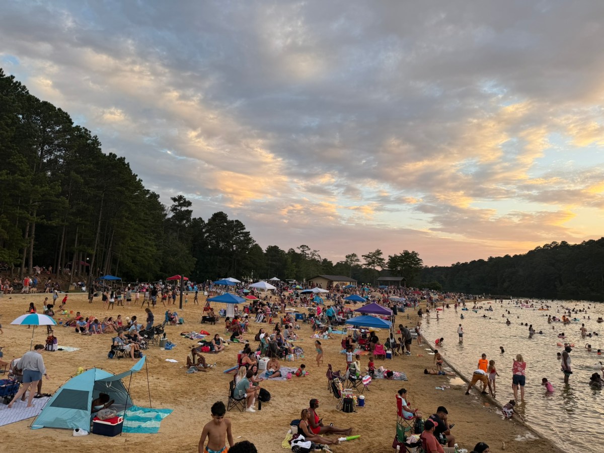 Crowds gather on the sandy beach and swim in the lake at Oak Mountain State Park during Fire on the Water at sunset