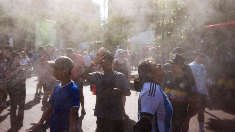 People stay cool as a large fan sprays water at FIFA Fan Festival at Boston City Hall Plaza in Boston.