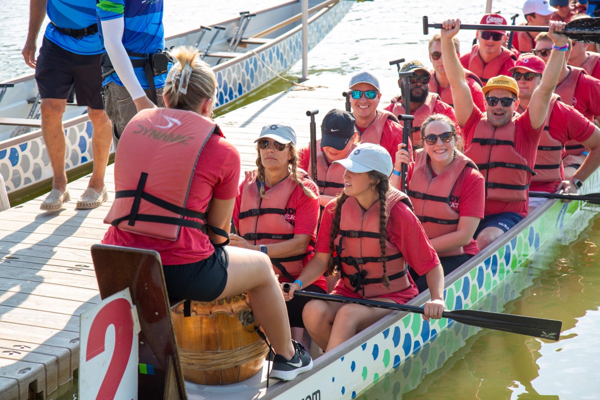 Team in matching red shirts and life jackets seated in a dragon boat at East Lake Park, ready to race at the Mitchell's Place Dragon Boat Festival