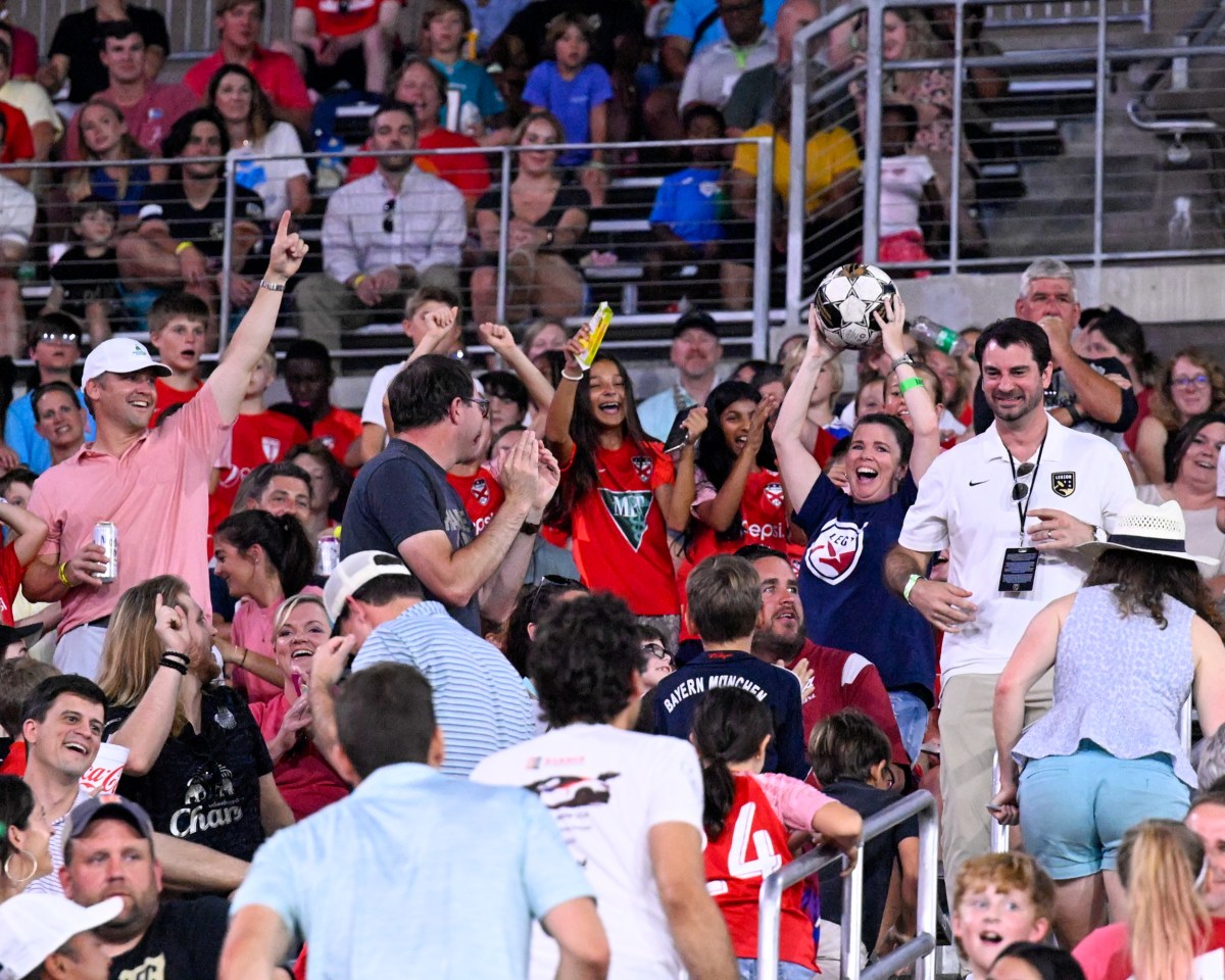 Excited Birmingham Legion fans cheer in the stands at Protective Stadium, one fan holding up a soccer ball