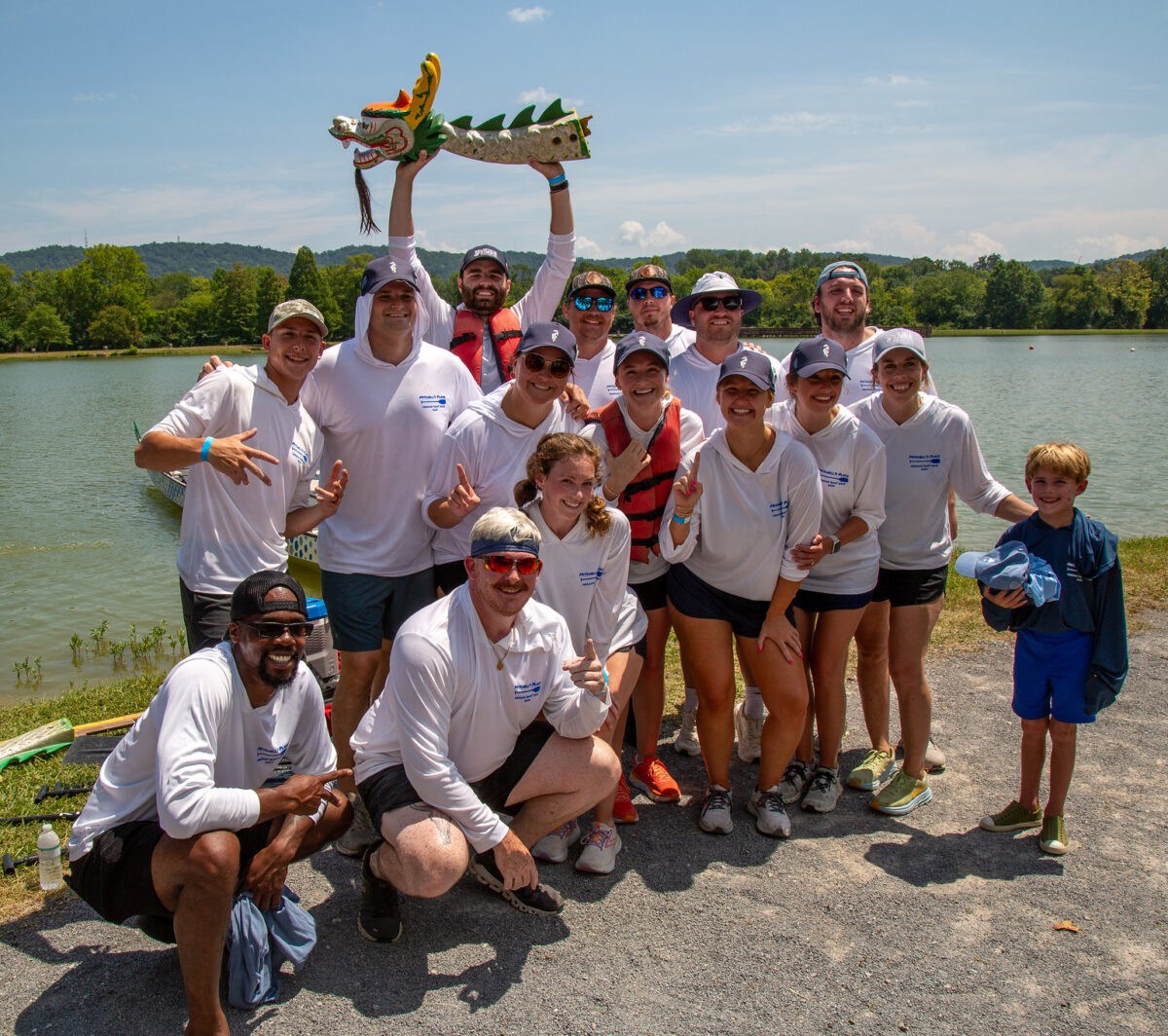 A Mitchell's Place dragon boat team poses together at East Lake Park, one member holding up a decorative dragon boat figurine