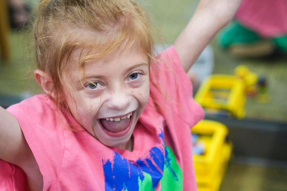 Little girl in pink shirt smiling at camera with arms up in the air