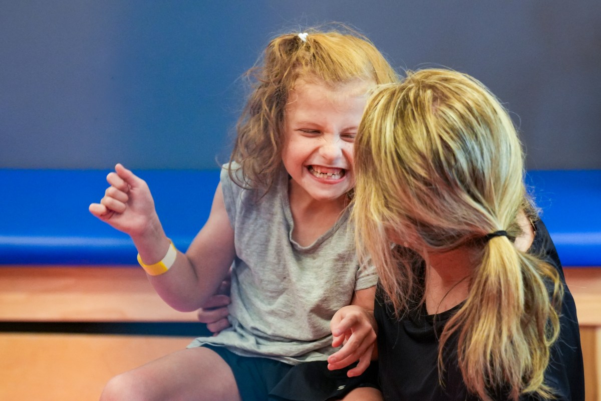 Little girl in grey shirt smiles at caregiver woman with ponytail
