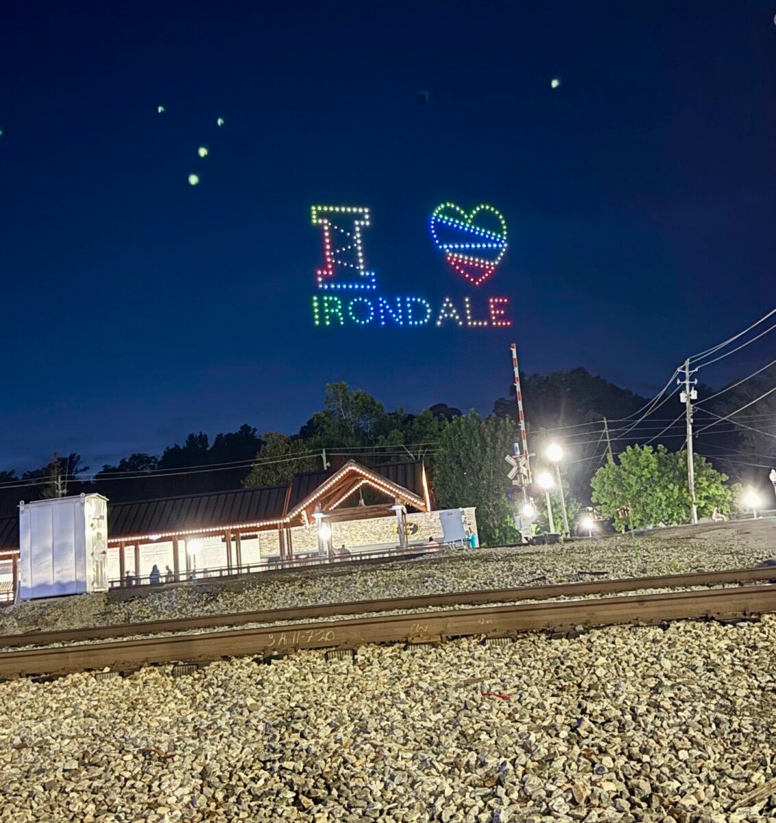 FREE I Love Irondale Day 2026 brings food, fun + tech 7 Drones forming the lit message I Heart Irondale in the night sky above railroad tracks and a lit building