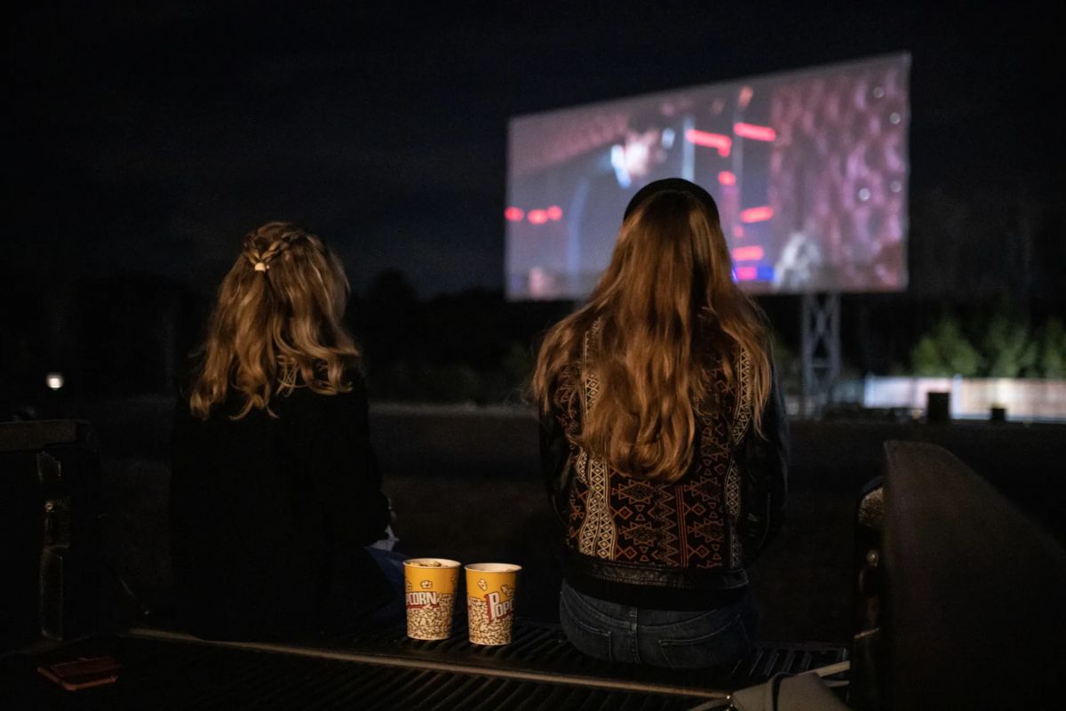 Two people sit in a truck bed with popcorn, watching a movie on the big screen at Grand River Drive-In