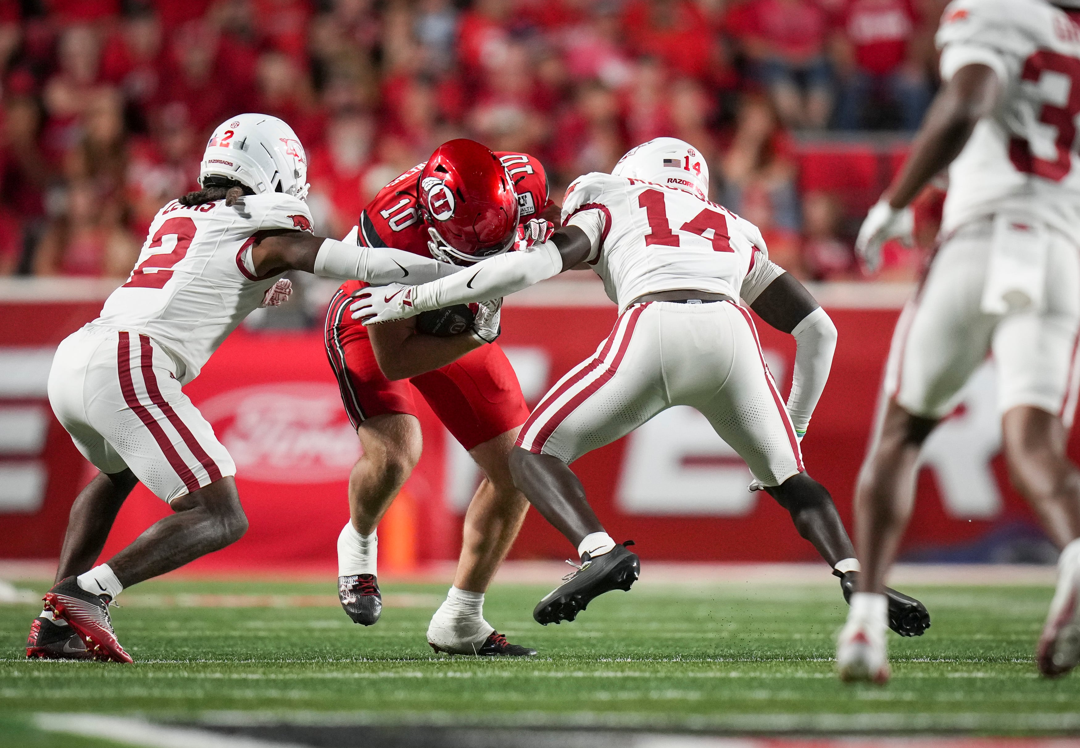 (Bethany Baker  |  The Salt Lake Tribune) Arkansas Razorbacks defensive back Kyeaure Magloire (14) and defensive back Shelton Lewis (2) tackle Utah Utes tight end Hunter Andrews (10) during the game between the Utah Utes and the Arkansas Razorbacks in Salt Lake City on Saturday, Sept. 12, 2026.