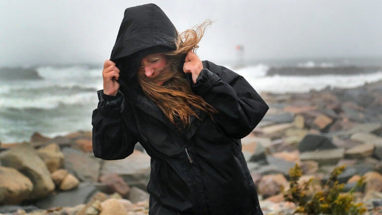 A woman in a black raincoat braces in the wind.