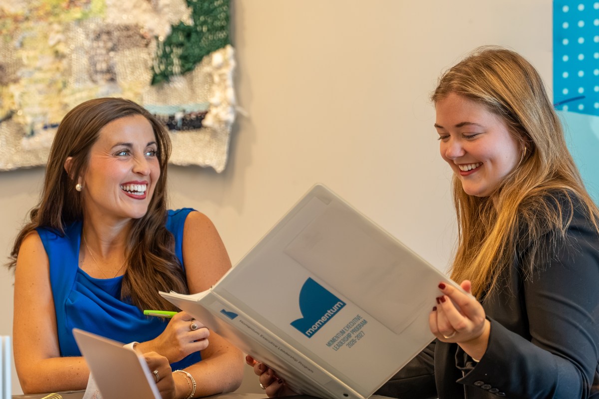 two women look at Momentum Leaders promotional materials and smile