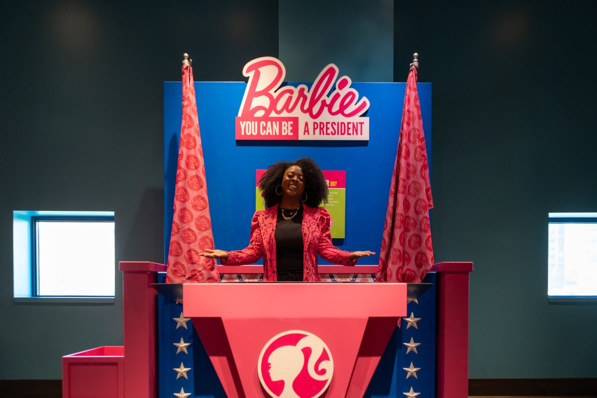 Woman poses at a podium reading "Barbie You Can Be A President" in the exhibit's leadership-themed career area